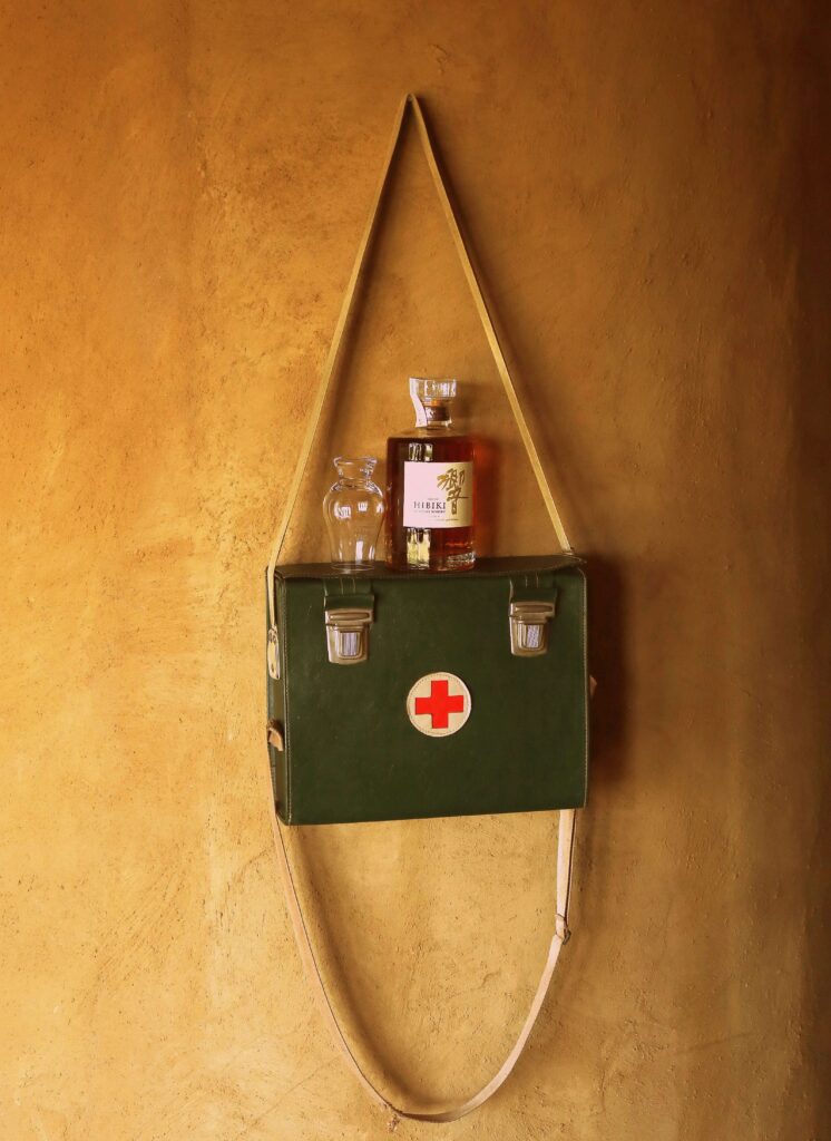 Maleta médica pendurada na parede com frasco de medicamento e copo ao lado, representando doenças, tratamento e benefícios por incapacidade no INSS.