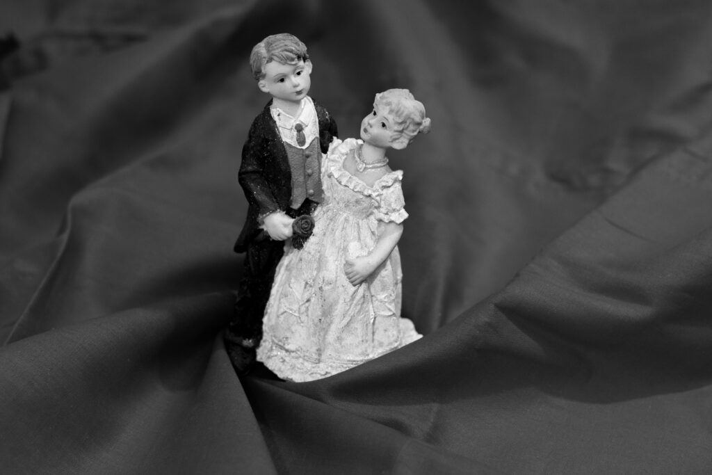 Miniatura de um casal de noivos sobre tecido escuro, simbolizando casamento, separação e processos de divórcio.