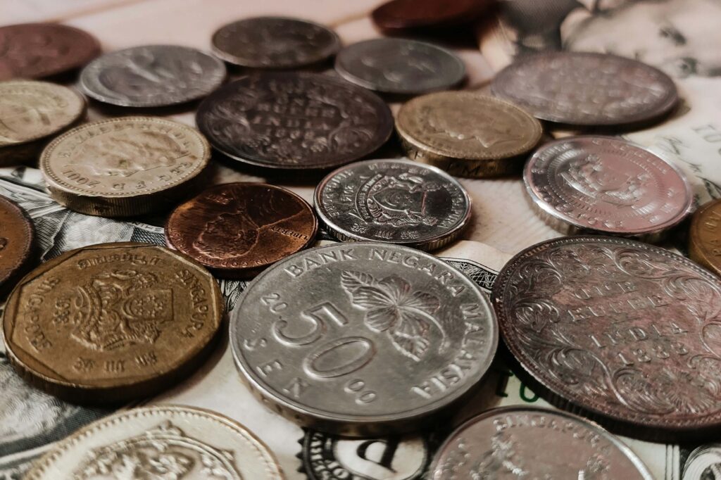 Diversas moedas de diferentes países e valores espalhadas sobre cédulas de dinheiro, simbolizando o impacto financeiro, o controle de gastos e os valores cobrados incorretamente em casos de cobrança indevida.