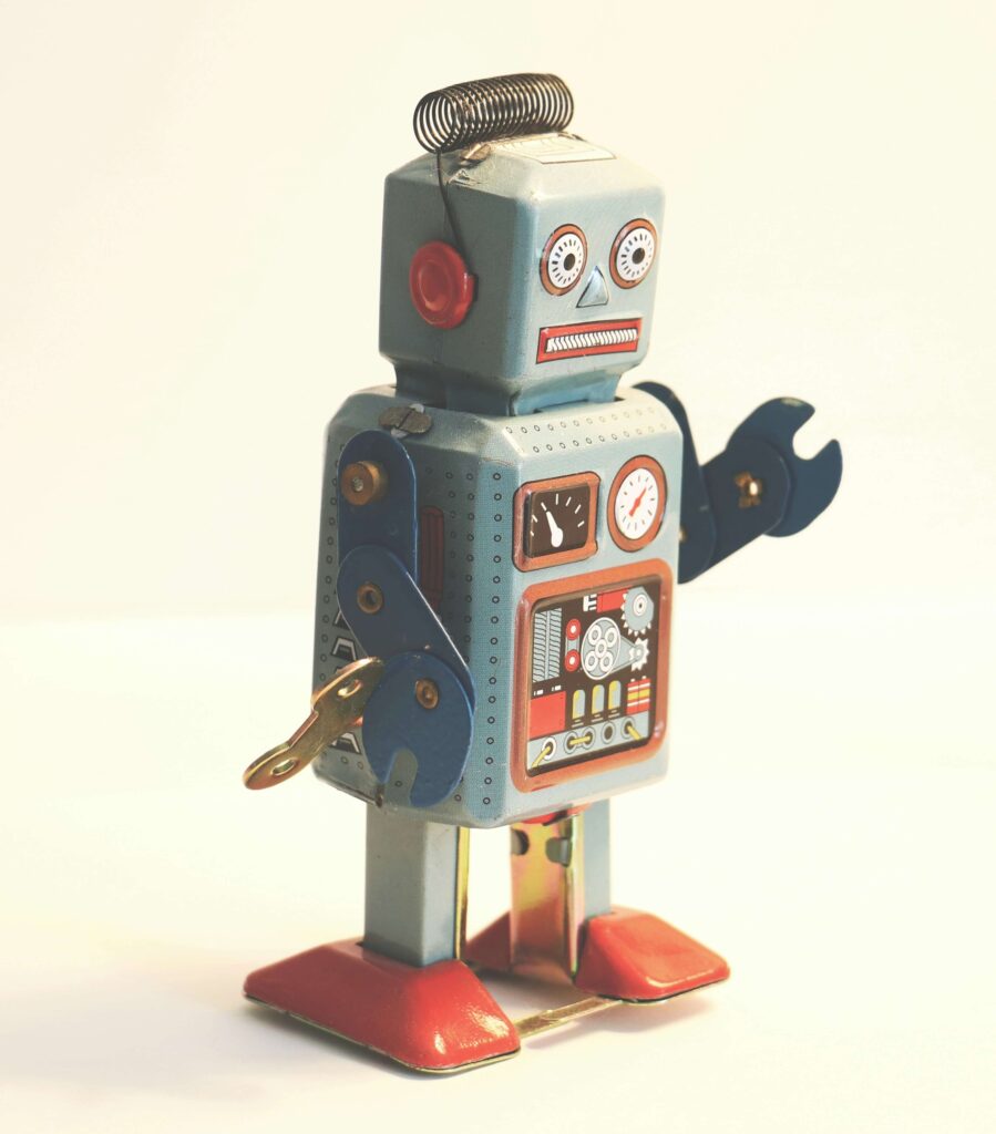Robô de brinquedo de lata antigo nas cores azul, vermelho e dourado, com uma chave de corda na lateral, simbolizando a infância, o desenvolvimento infantil e o direito à educação básica e vaga em creche.