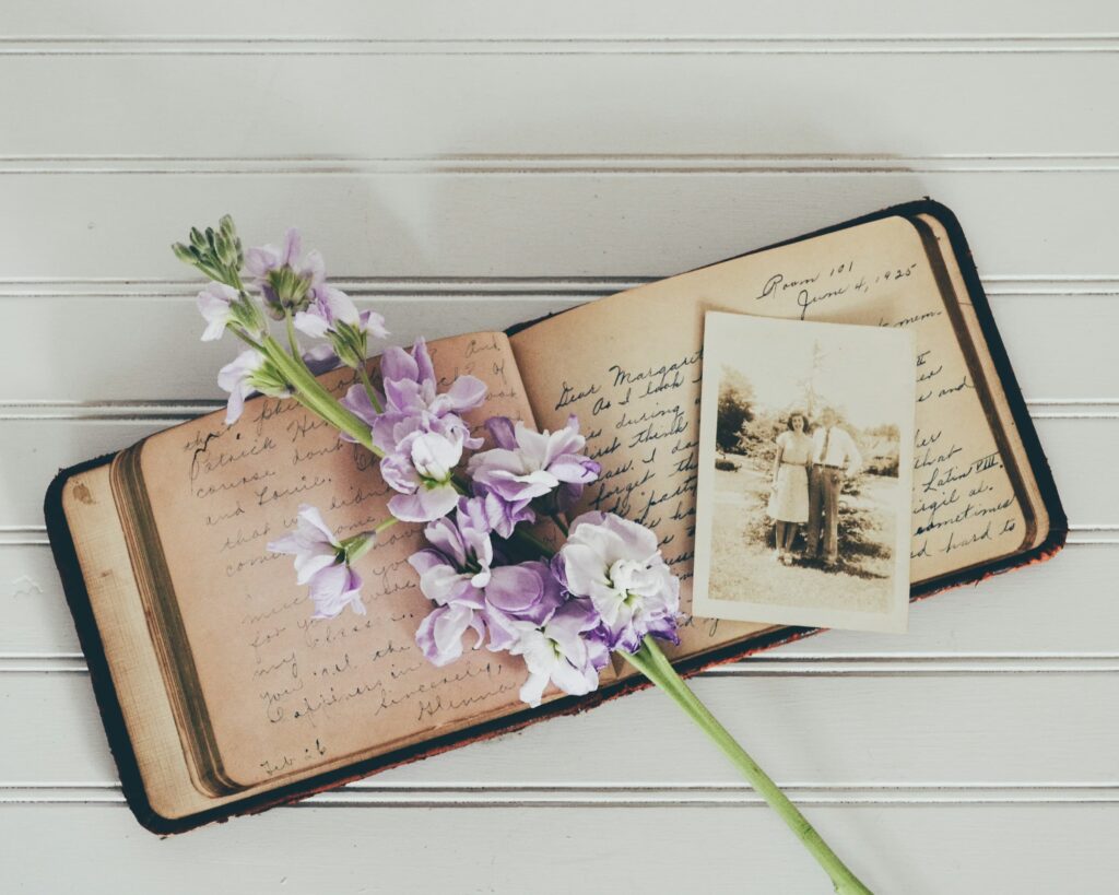 Diário antigo manuscrito com flores lilás e uma fotografia em preto e branco de um casal, evocando memória e cuidado familiar, tema ligado à interdição de um idoso.