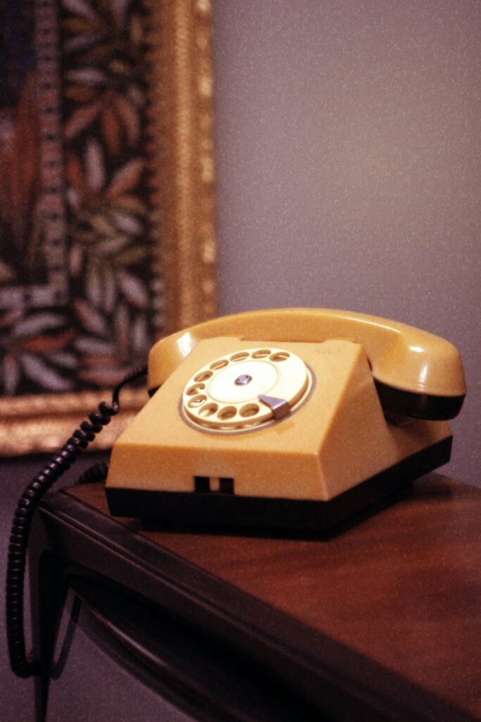 Telefone antigo de disco, na cor amarelo mostarda, sobre uma mesa de madeira ao lado de uma moldura dourada, remetendo à comunicação familiar e ao tema da interdição de um idoso.